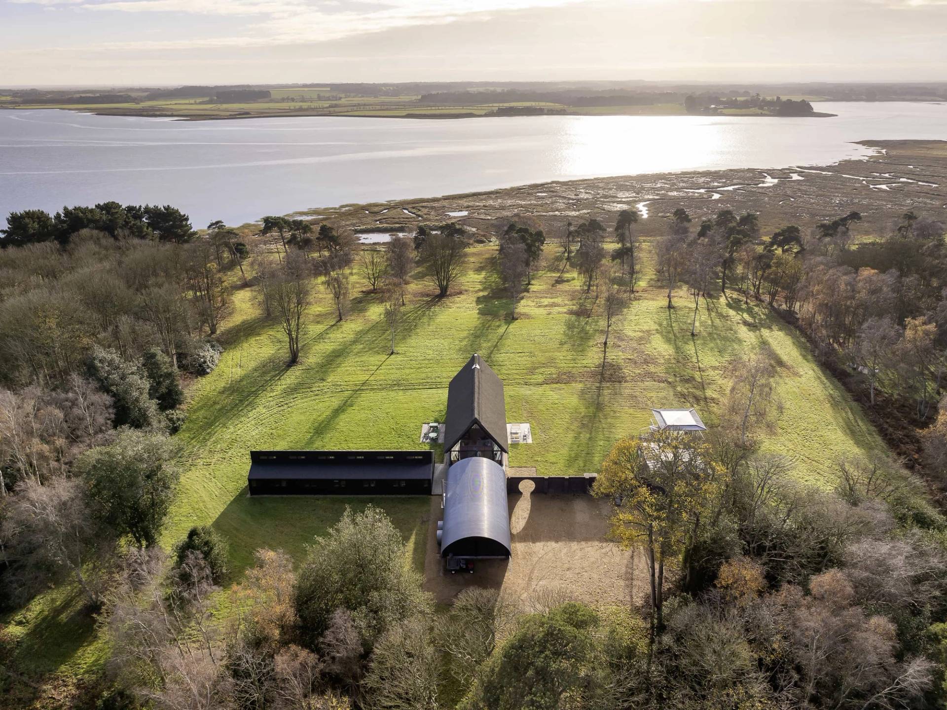High-altitude aerial drone shot of a modern architectural longhouse estate set in coastal Suffolk grounds, Love Locations IP17.