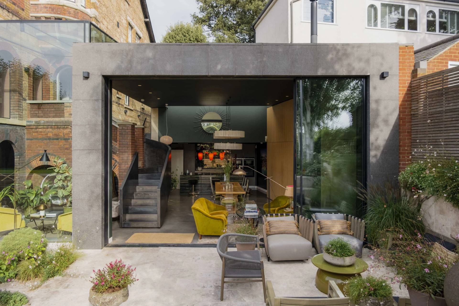 Symmetrical exterior shot looking into a modern dark frame glass extension from a paved outdoor garden patio, ideal for commercial film backdrops, Love Locations.
