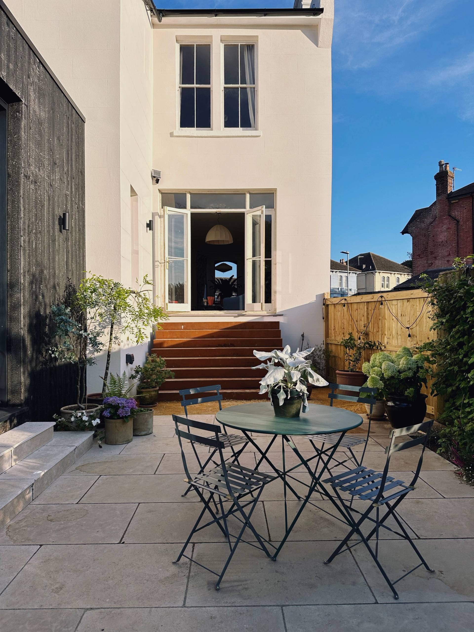 Rear exterior paved terrace featuring dark metal bistro seating set against a white render facade in Hastings, ideal for summer lifestyle shoots, Love Locations TN34.