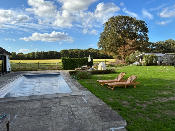 Outdoor terrace and private swimming pool film location in Essex CM4 by Love Locations, featuring stone paving, sun loungers, and expansive green lawn views under a blue sky.