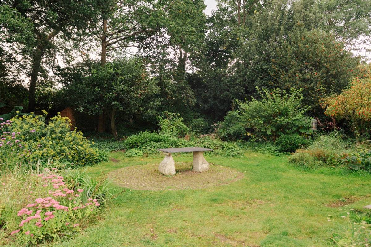 Rustic stone garden bench set on a round lawn surrounded by woodland foliage, ideal for outdoor furniture lookbooks, Love Locations SE15.