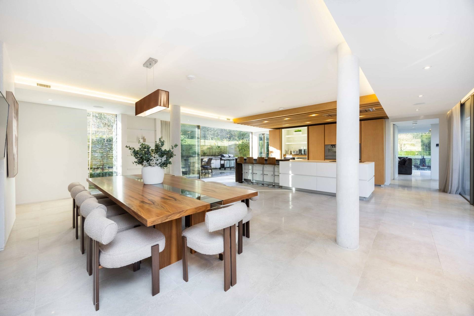 Contemporary luxury kitchen location in Radlett, WD7 featuring a solid wood dining table, white island, and timber ceiling slats via Love Locations.