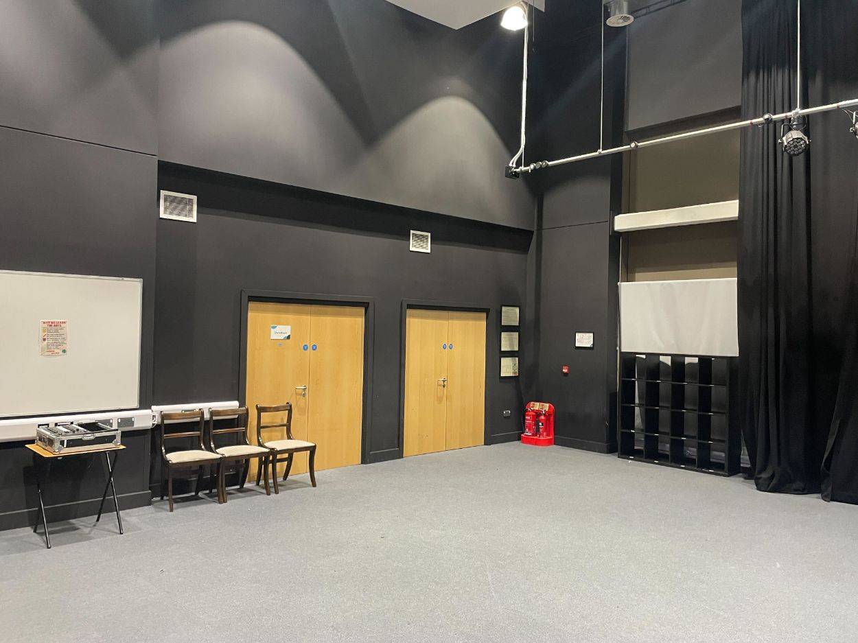 Love Locations production staging room RG30: Industrial dark-painted performance hall corner with double exit doors and storage lockers, ideal for backstage scenes and short films.