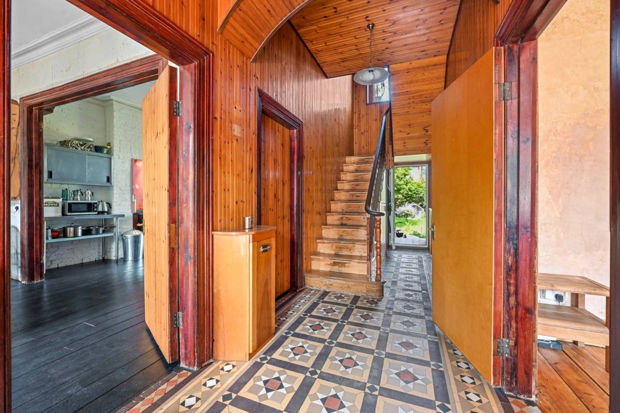 Retro entrance hallway featuring pine wood panelled walls, patterned floor tiles, and timber staircase, ideal for character film scenes, Love Locations E7.