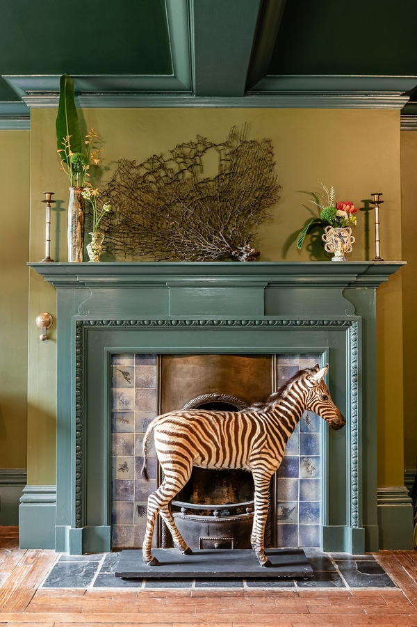Quirky mantelpiece display featuring a decorative zebra prop against muted green walls, an artistic brand photoshoot setting from Love Locations.