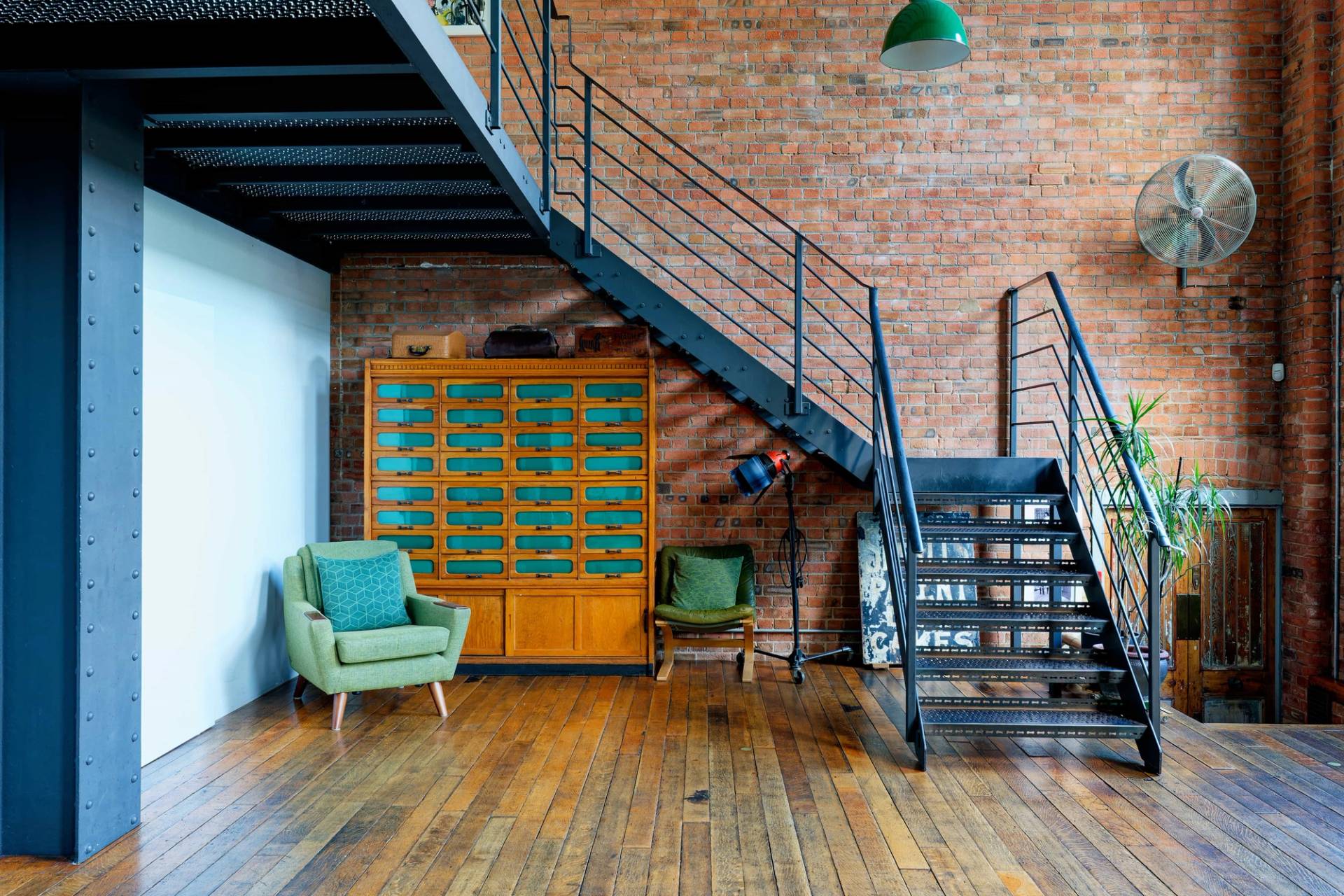 Under-stair alcove featuring a yellow vintage plan chest unit, green armchair, and industrial steel staircase in East London, Love Locations.