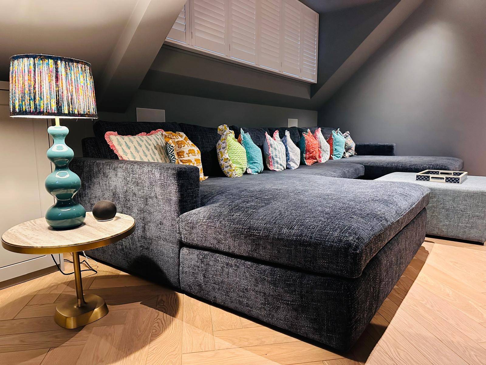 Cozy attic media room with a large dark grey L-shaped sectional sofa and colorful cushions, Love Locations TW11.