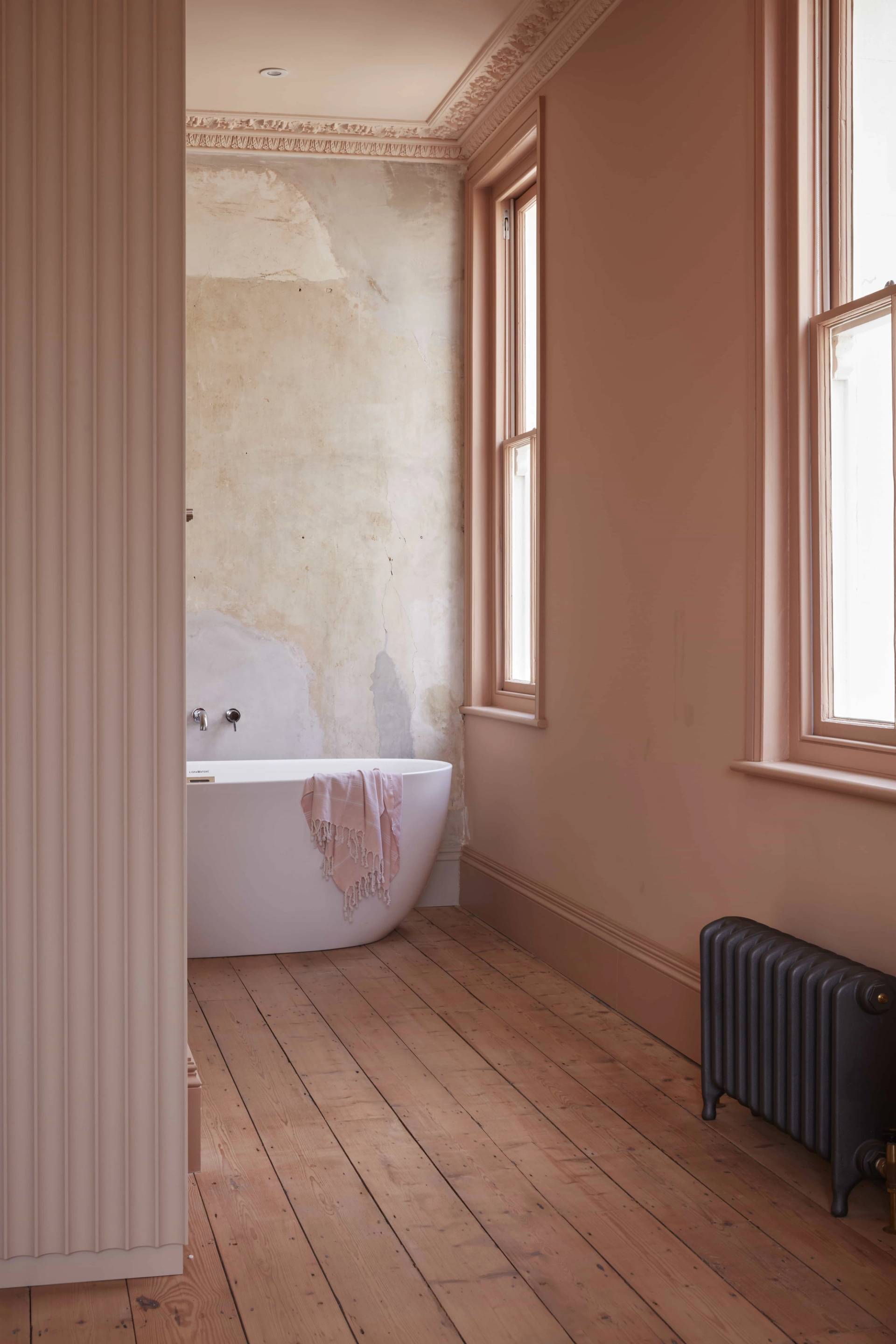 Freestanding bath tub positioned between pink plaster walls and wooden sash windows, Love Locations.