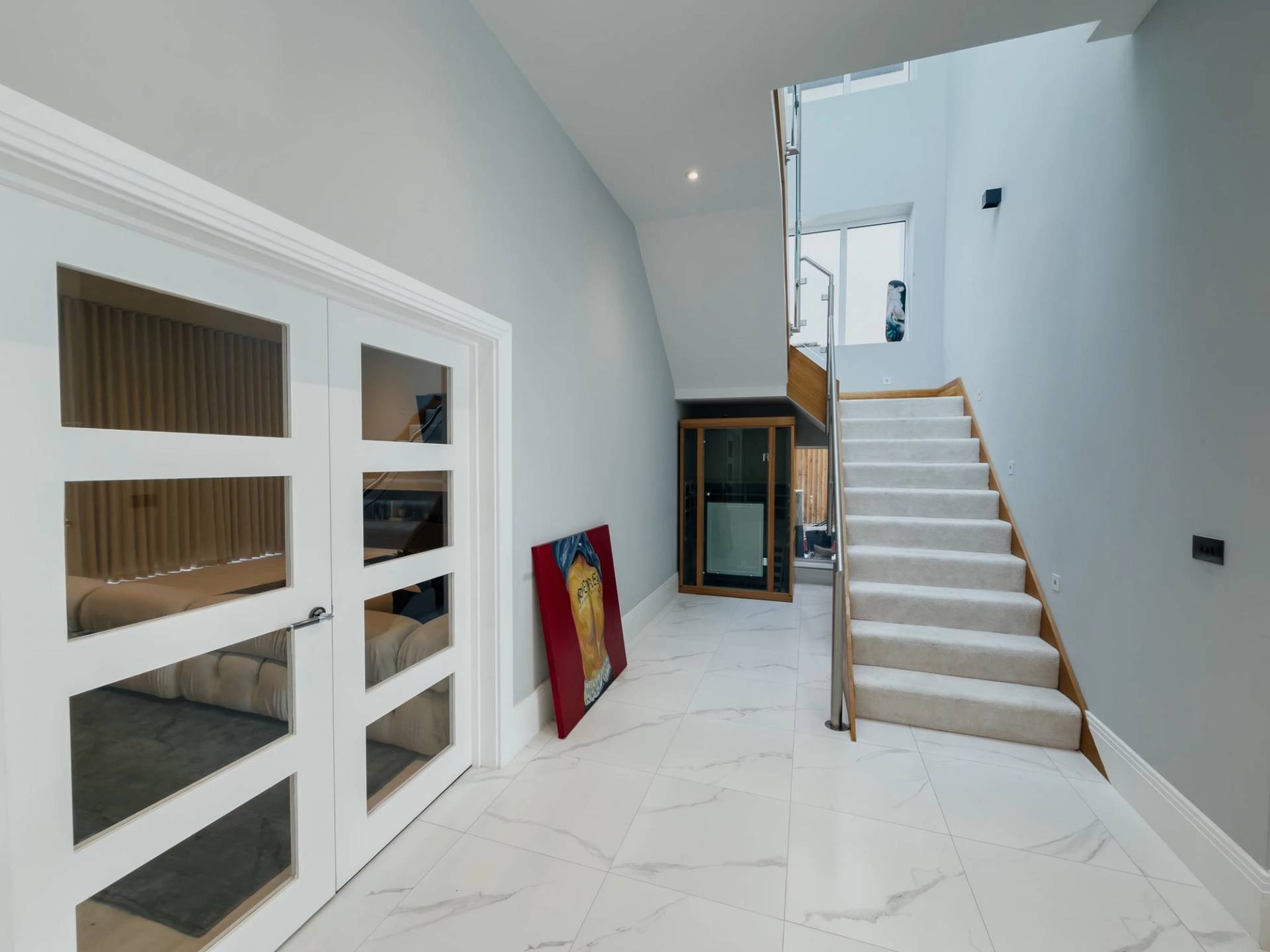 Grand entrance hallway and foyer location house in Barnet EN4 from Love Locations, displaying white marble tile flooring, double glass entry doors, and a carpeted staircase.