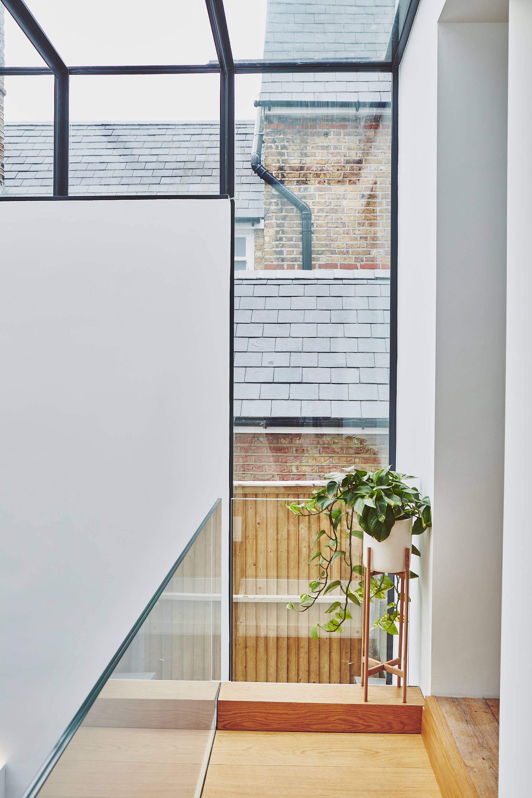 Glass walkway transition looking past potted indoor plants towards full-height glass window panes, Love Locations TW1.