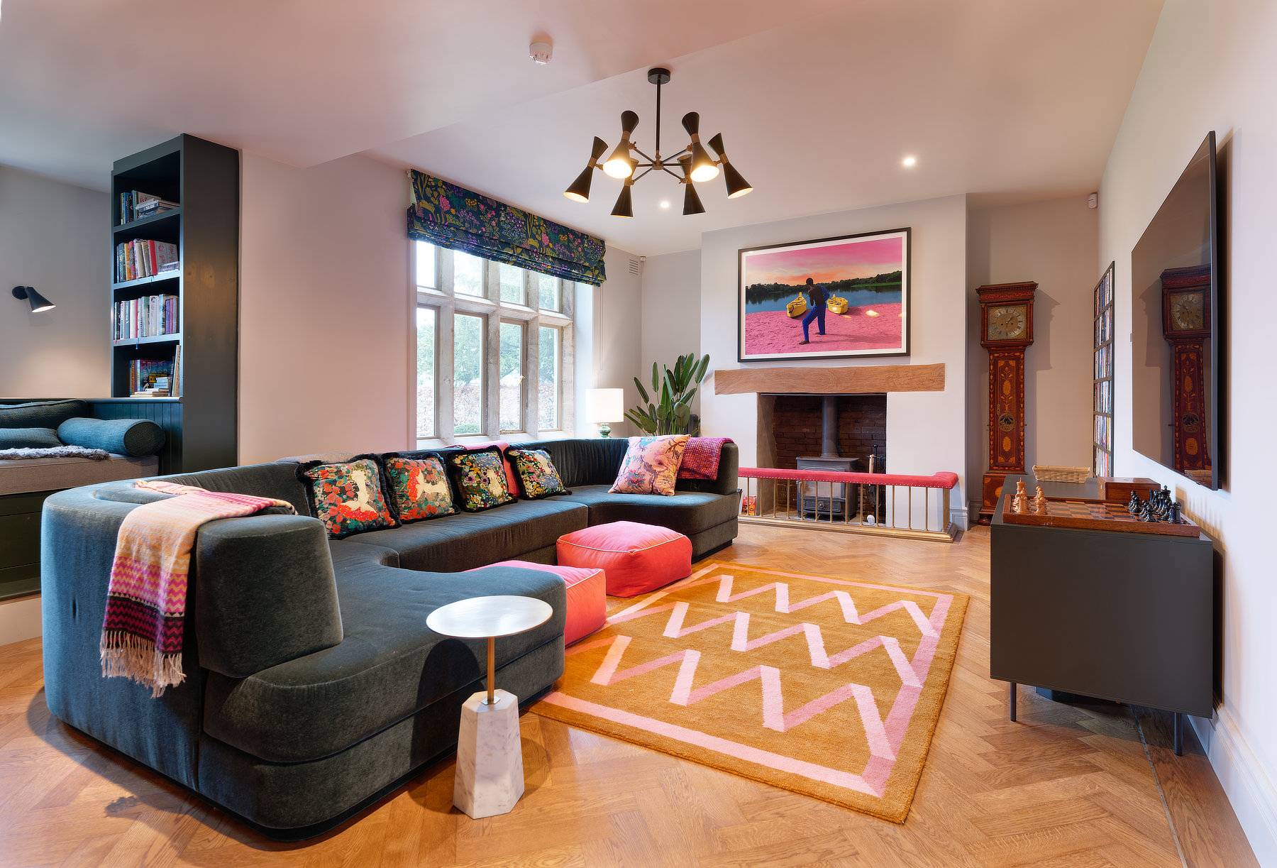 Spacious living room featuring a dark green sectional sofa, orange geometric rug, and open fireplace, Love Locations OX7.