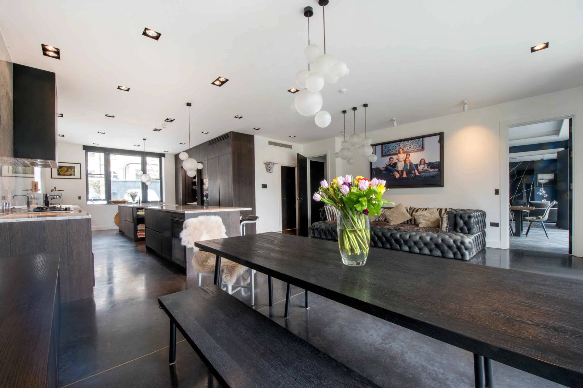 Spacious kitchen dining zone styled with a minimalist wooden table, bench seating, and fresh floral centerpieces, Love Locations.