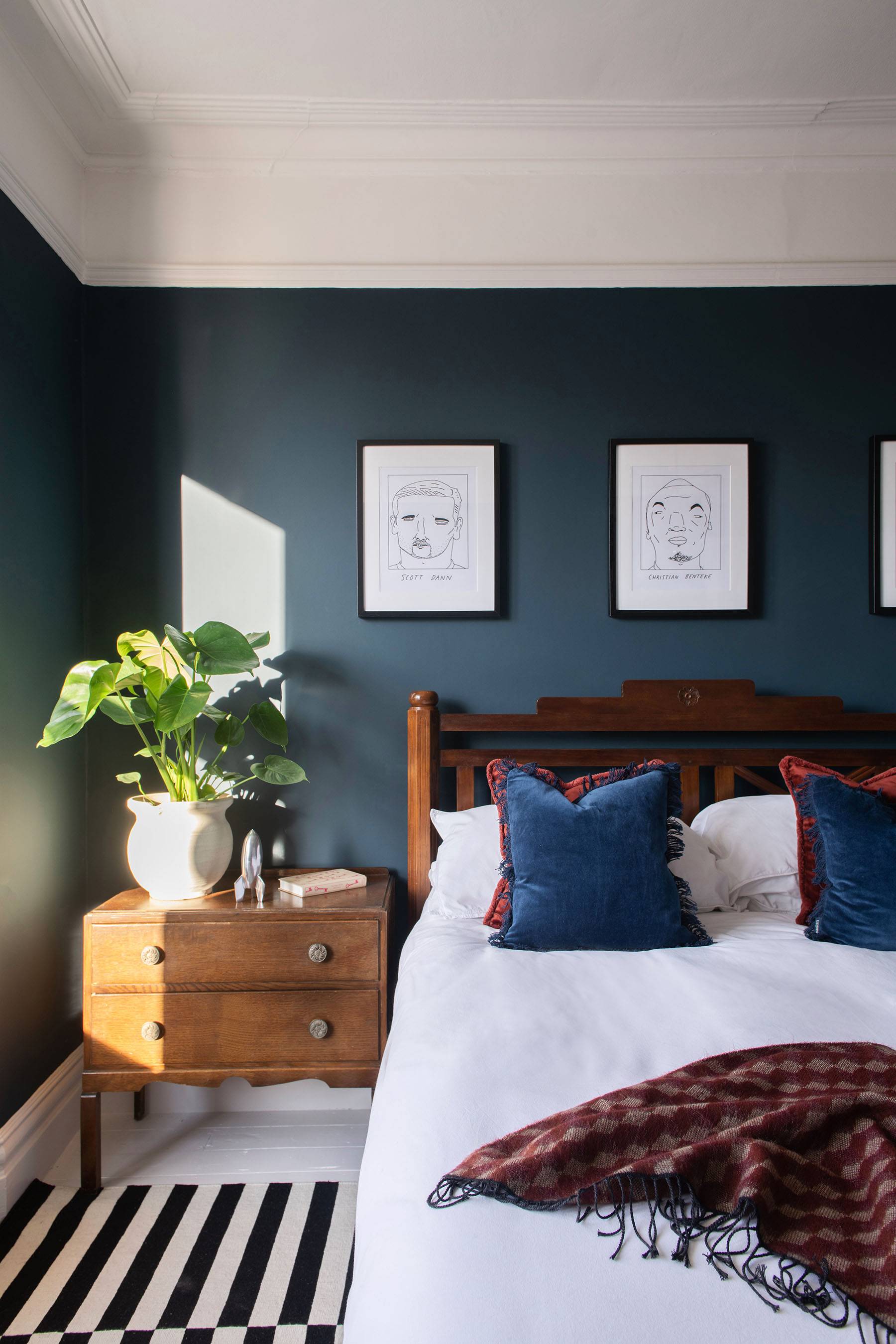 Spacious dark teal bedroom with bay windows, black and white striped area rug, and overhead spider chandelier, Love Locations.