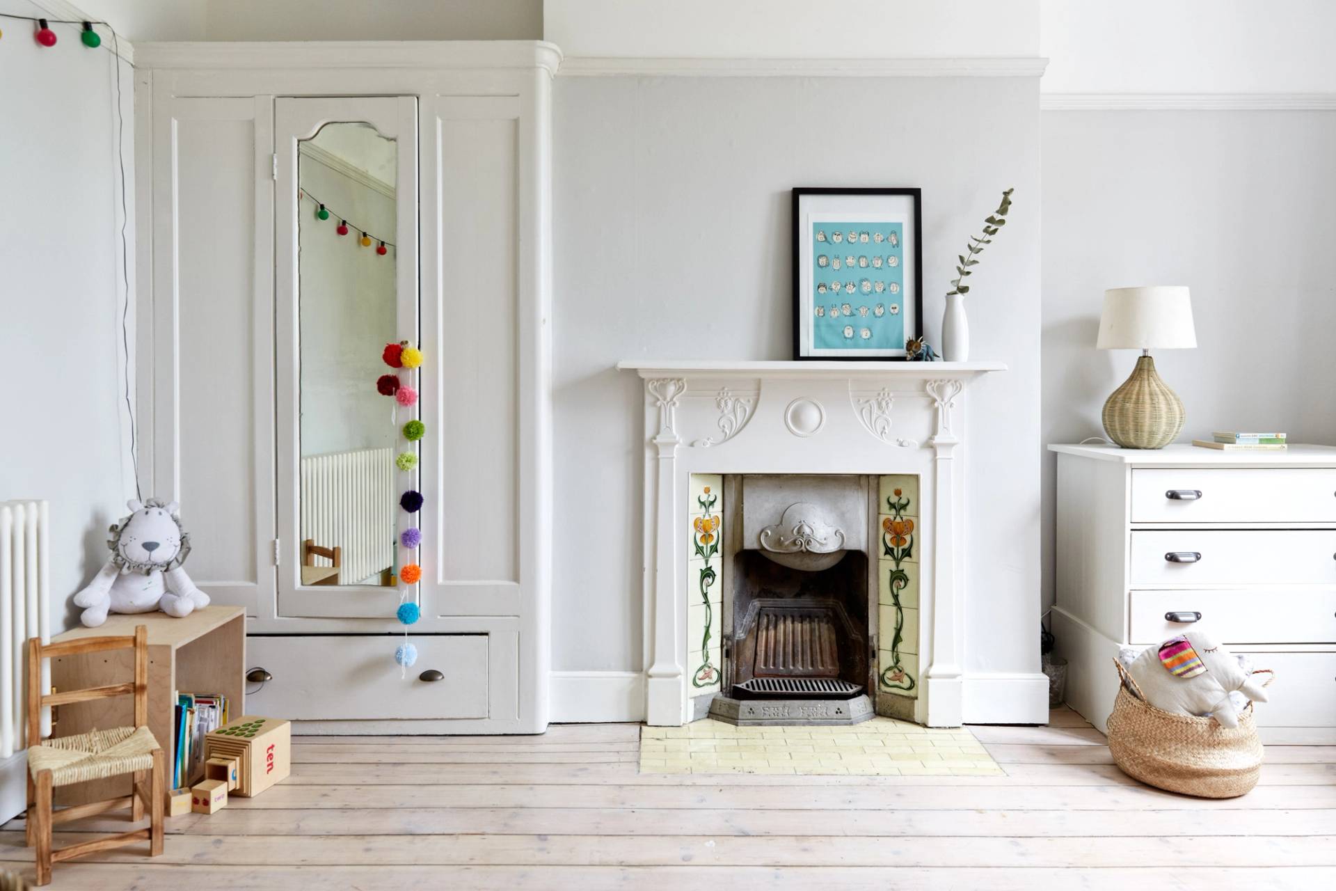Bright bedroom with a period fireplace, floral tiled hearth, white wardrobe, and whitewashed timber floorboards, Love Locations N13.