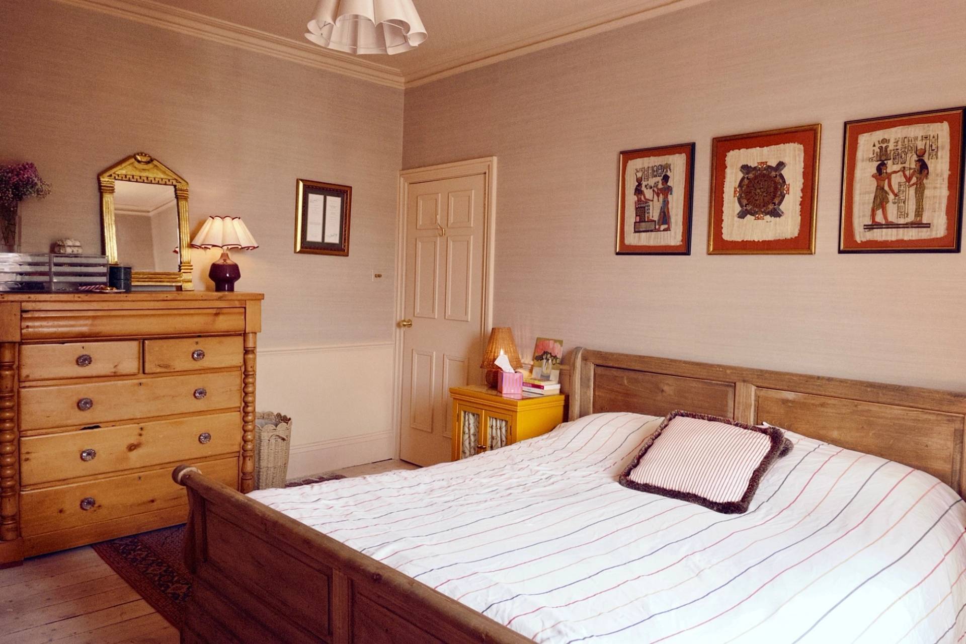 Classic bedroom interior featuring a dark wooden bed frame and framed vintage artwork on neutral walls, Love Locations.