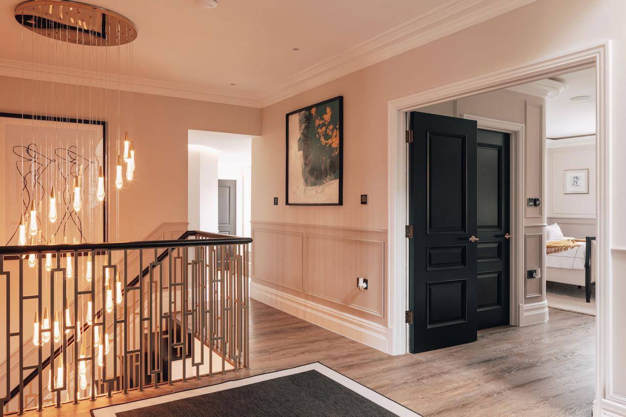 Upper floor hallway landing with warm wall sconce lighting, dark doors, and panelled walls, Love Locations W5.