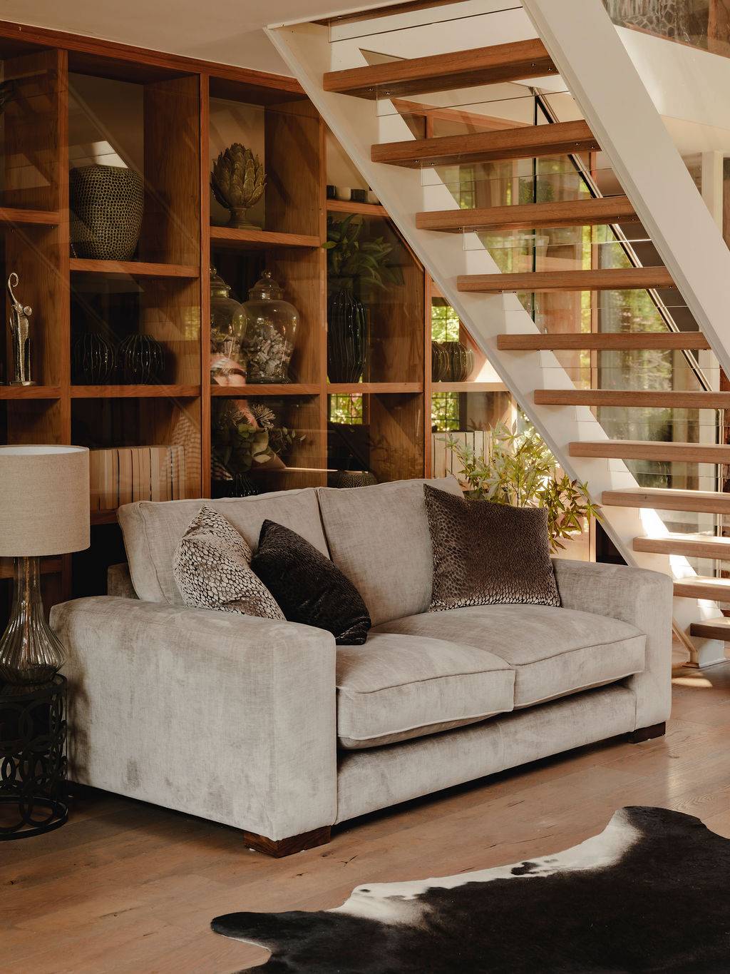 Under-stairs seating area with a neutral cream sofa set against custom oak bookshelf display units, ideal for domestic lifestyle brand shoots, Love Locations RG9.