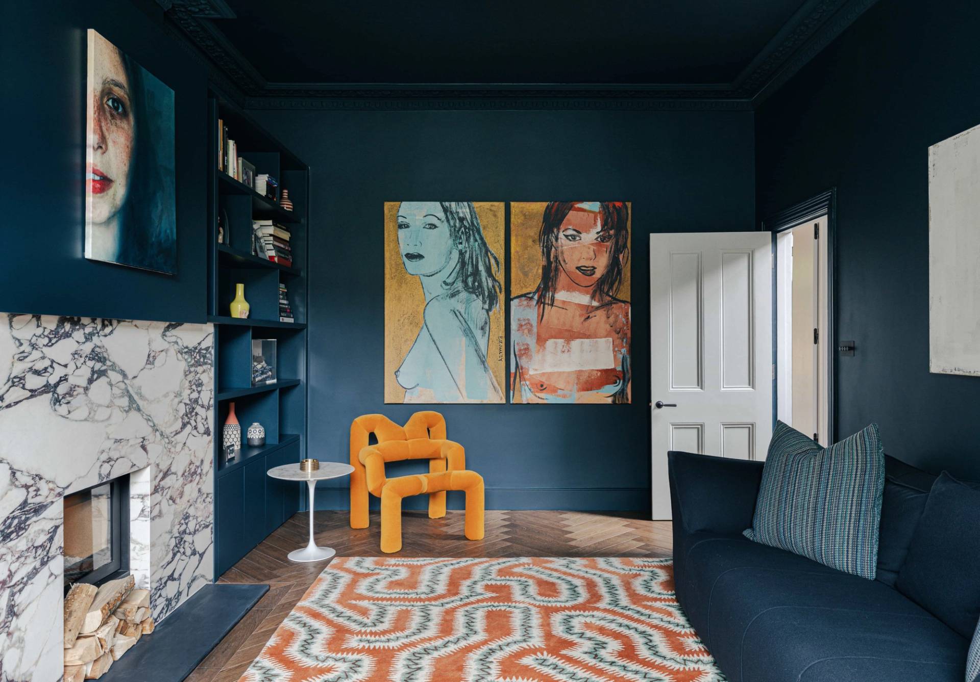 Atmospheric deep blue library room featuring bold modern artwork, orange tube chair, and geometric rug, ideal for fashion editorial shoots, Love Locations.