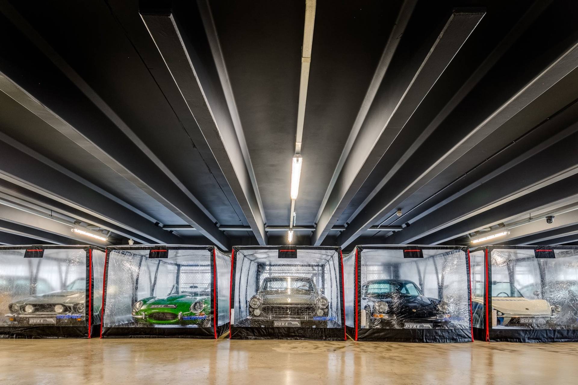 : Front view of classic vintage cars in clear protective bubbles inside a 1950s Brentford factory location through Love Locations.