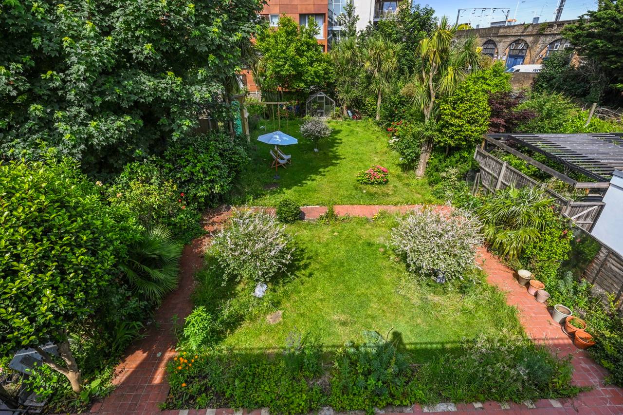 High-angle bird's-eye view of a long green lawn garden and brick patio terrace in Newham, Love Locations.