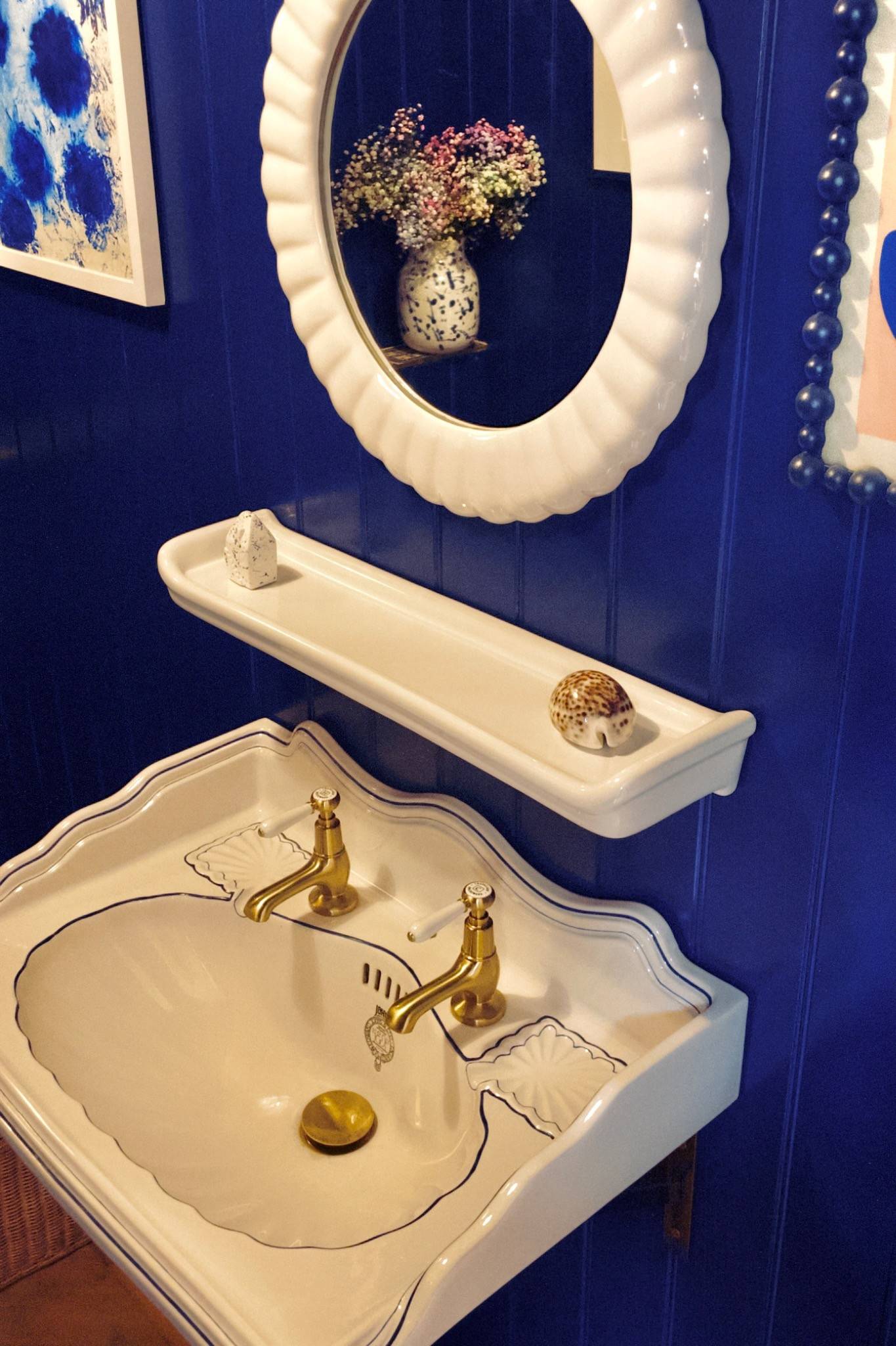 Close-up of a luxury white wall-mounted basin with gleaming brass taps set against striking dark blue wood panel walls, Love Locations TW7.