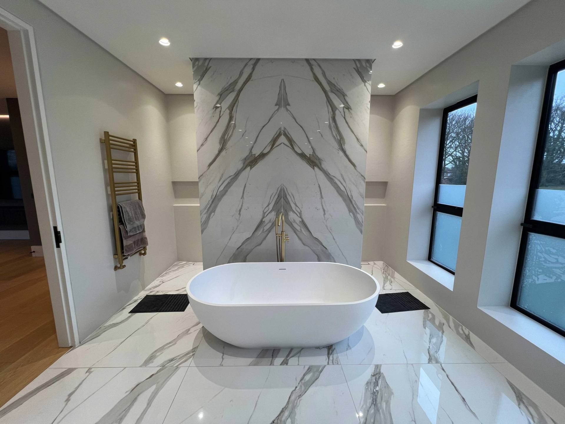 Luxury spa bathroom featuring a freestanding oval tub set against a dramatic book-matched Calacatta marble slab wall, perfect for skincare brand commercials, Love Locations N3.
