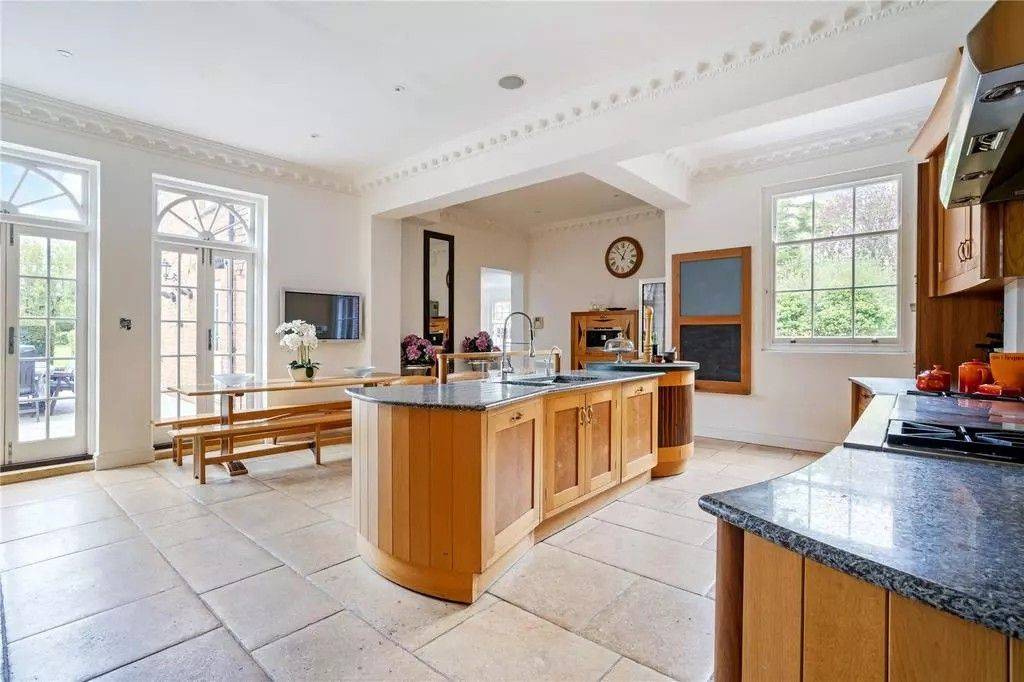 Spacious country house kitchen shoot location featuring a rounded wooden island counter, flagstone flooring, and arched French doors via Love Locations.
