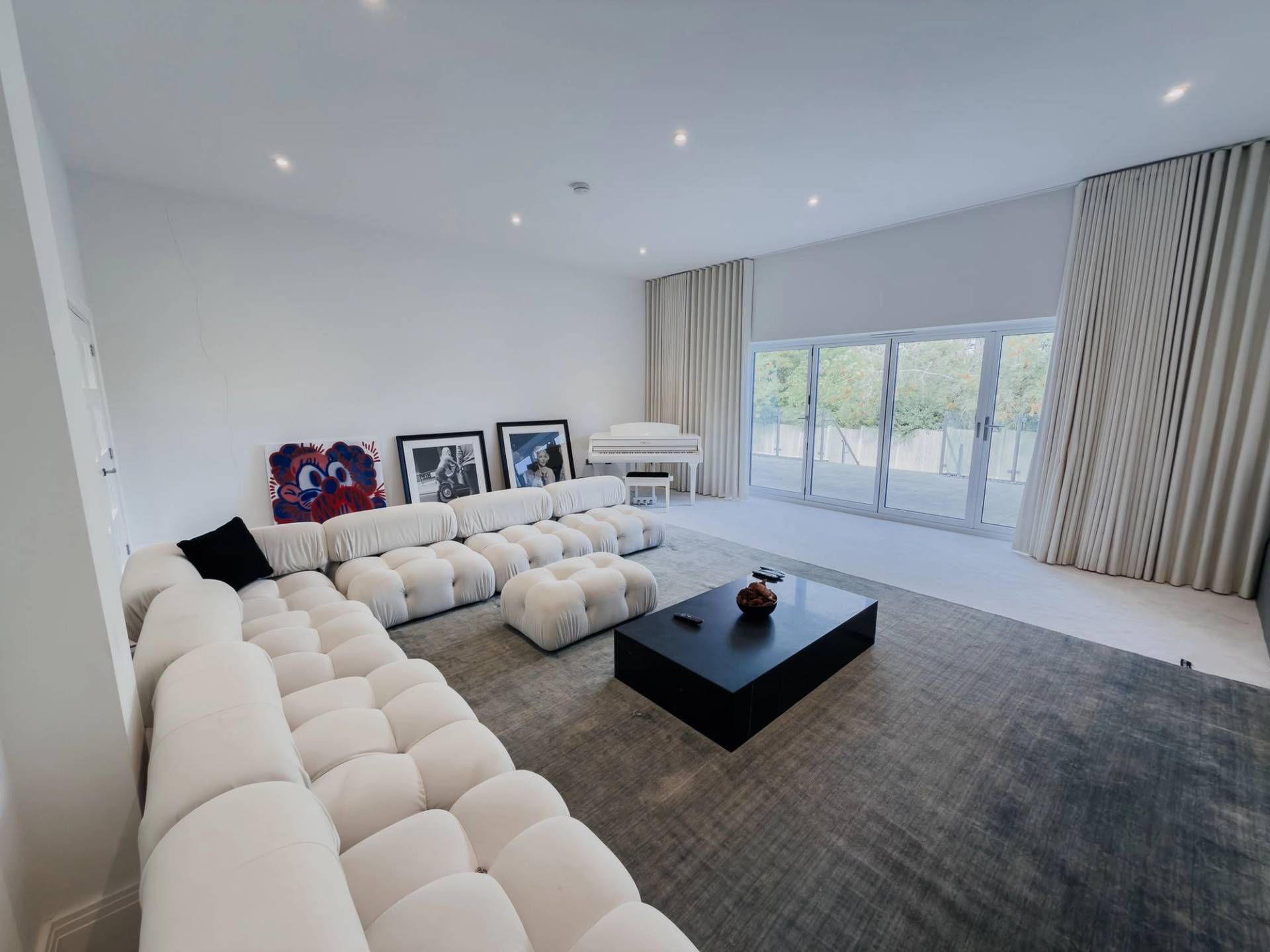 Luxurious contemporary living room photoshoot backdrop in Barnet EN4 through Love Locations, featuring a large cream modular sectional sofa, dark rug, and grand piano.