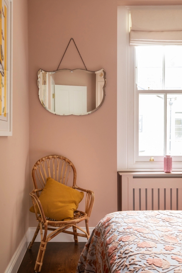 Soft pink bedroom corner shoot location in Westminster SW1V via Love Locations, featuring a classic scalloped wall mirror, a wicker armchair, and a vintage style radiator.