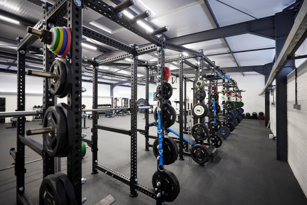 Extended line of professional squat racks and weightlifting stations inside a modern industrial gym facility, ideal for workout video filming, Love Locations.