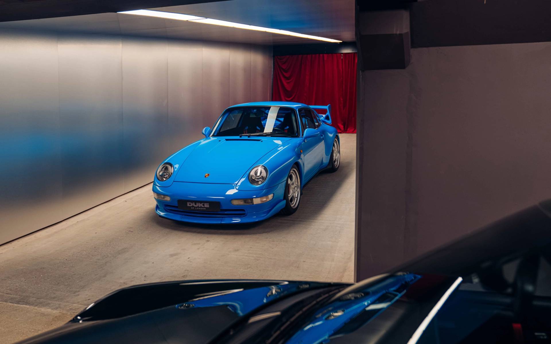 Bright blue Porsche Carrera RS parked under sleek overhead lighting strip in an underground driveway by Love Locations.