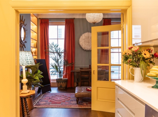 Sun-drenched open-plan living and dining space available for media production in Westminster SW1V through Love Locations, featuring warm yellow doors and red curtains.