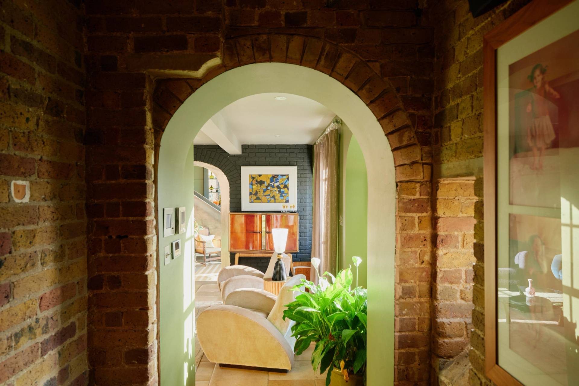 Brick archway doorway leading into a cozy sage green reception room with plush armchairs, Love Locations.