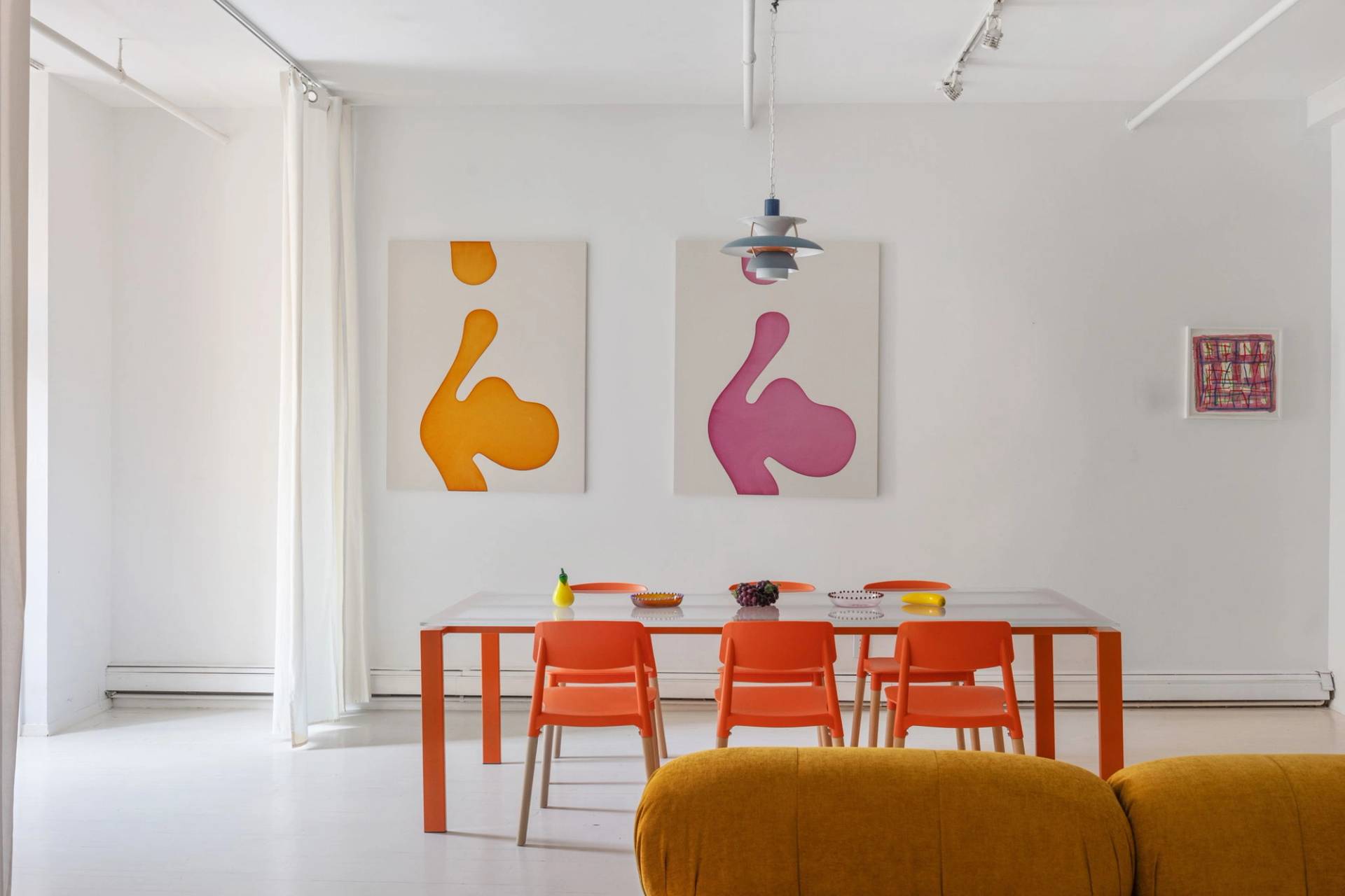 Vibrant dining space with an orange-legged dining table, orange dining chairs, and bold abstract art in a Tribeca NY 10007 loft location by Love Locations.