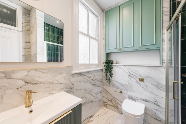 Luxury marble-tiled cloakroom bathroom with elegant sage green wall cabinets and gold fixtures, Love Locations North London.
