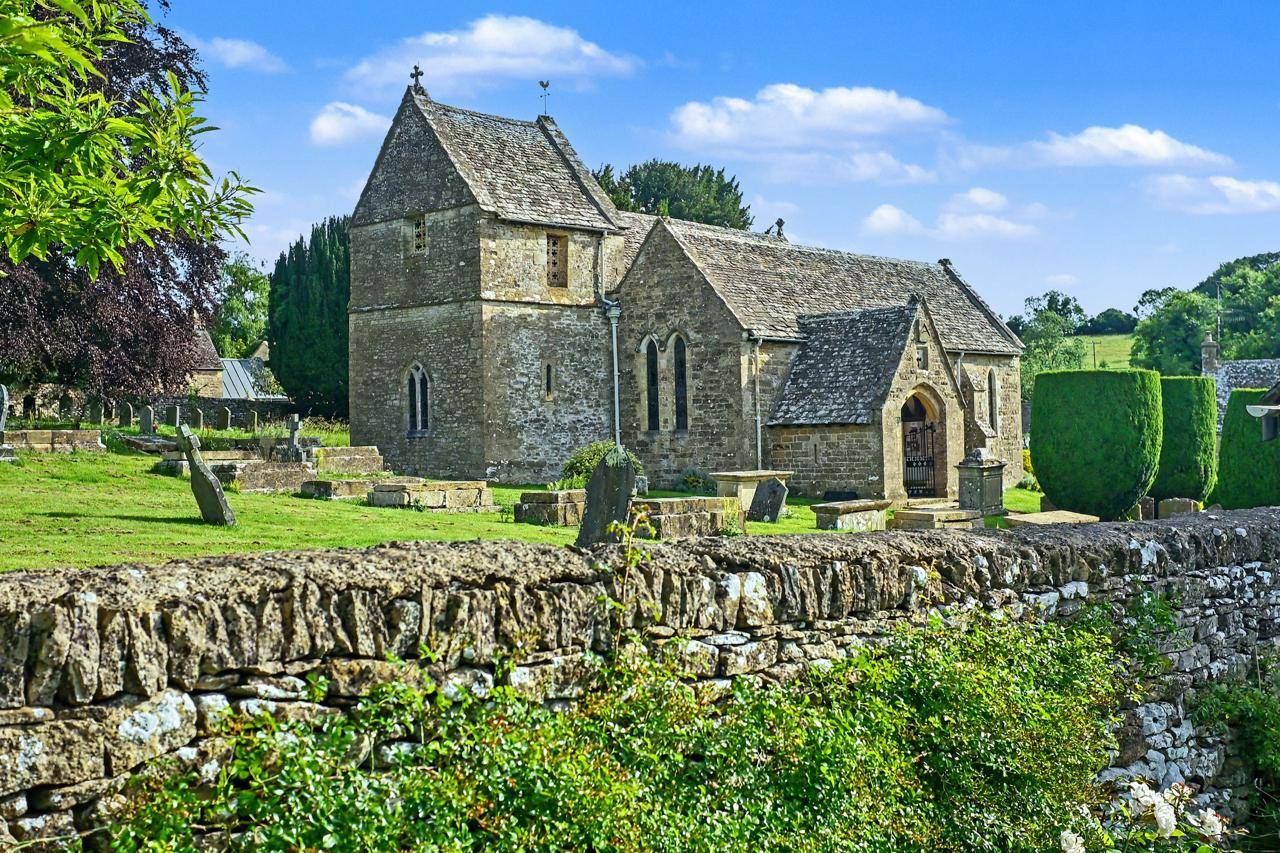 Traditional English village church film location in Gloucestershire GL7 by Love Locations, featuring weathered Cotswold stone masonry, churchyard headstones, and mature trees.