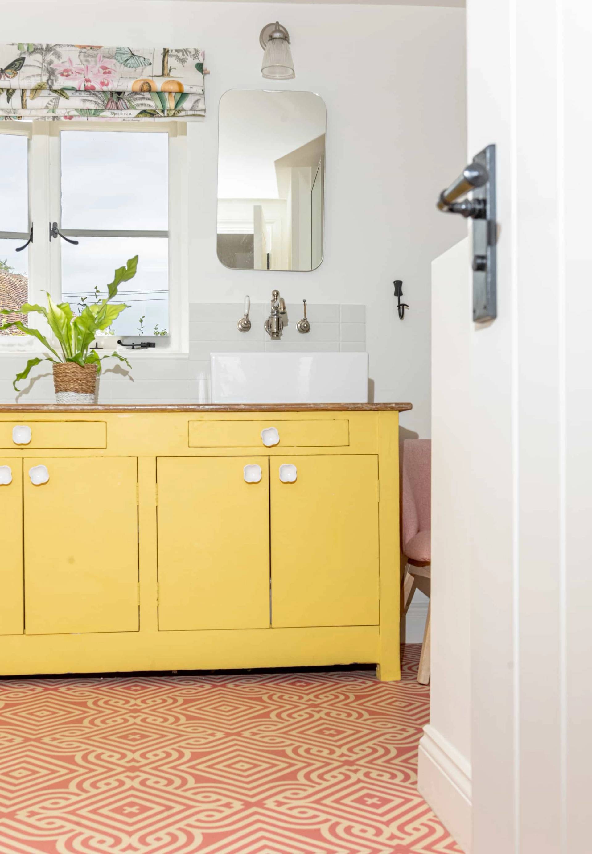 Yellow painted wooden bathroom vanity unit with double white sinks set against off-white walls, Love Locations GU28.