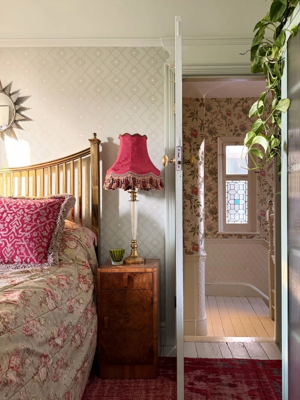 Cozy bedroom corner with brass bed frame, pink lampshade, and wallpapered doorway, Love Locations N13.