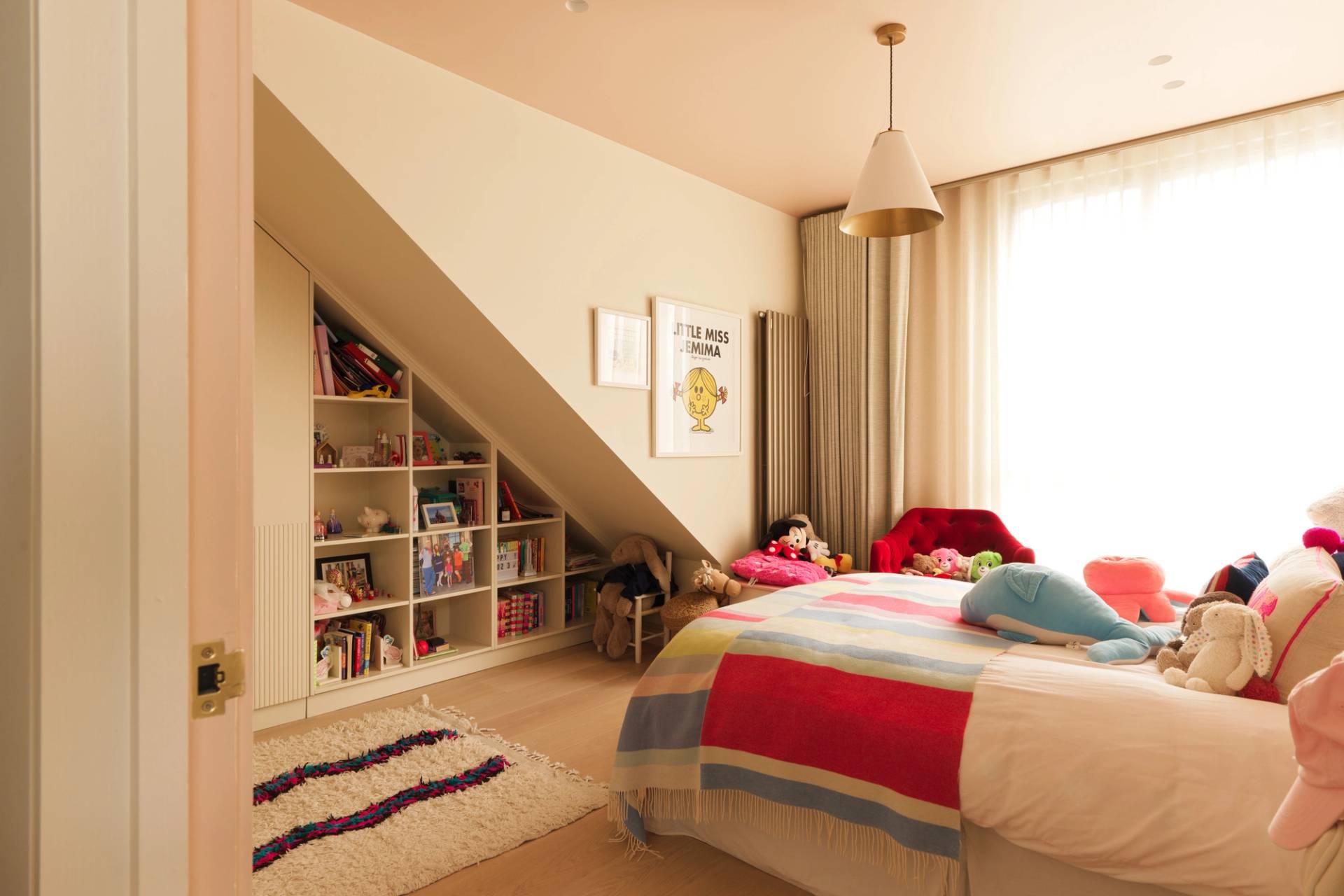 Playful attic bedroom nook with custom corner built-in shelving and dormer window by Love Locations.