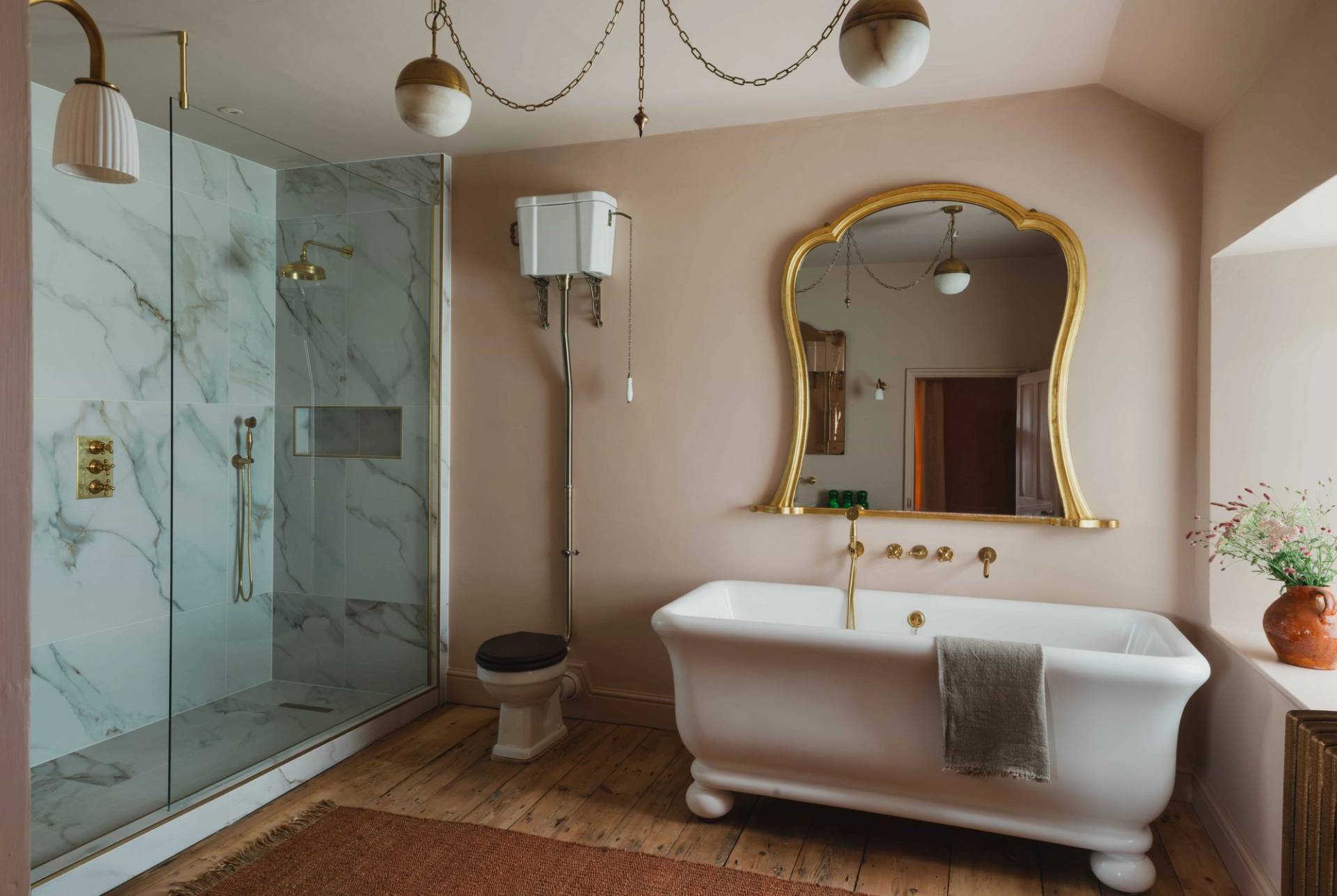 Elegant pink bathroom film location with a freestanding bathtub, glass walk-in shower, and gold mirror frame in Newquay from Love Locations.