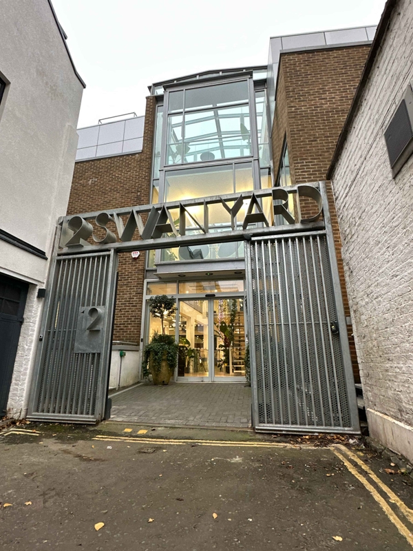 Outdoor entrance to Swan Yard featuring metal gates, a modern metal letter sign, and walkway leading to an industrial-style warehouse building.