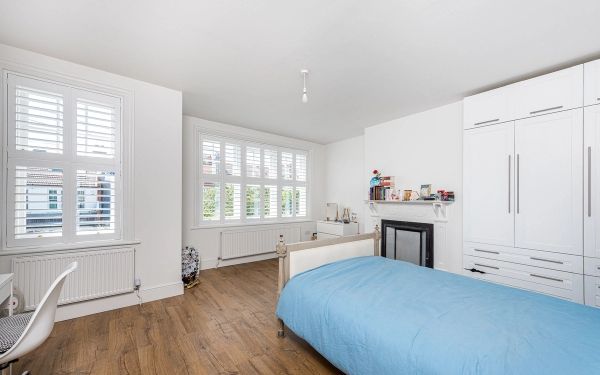 Bright double bedroom shoot space with clean white walls, window shutters, and a minimalist wooden bed frame, Love Locations.