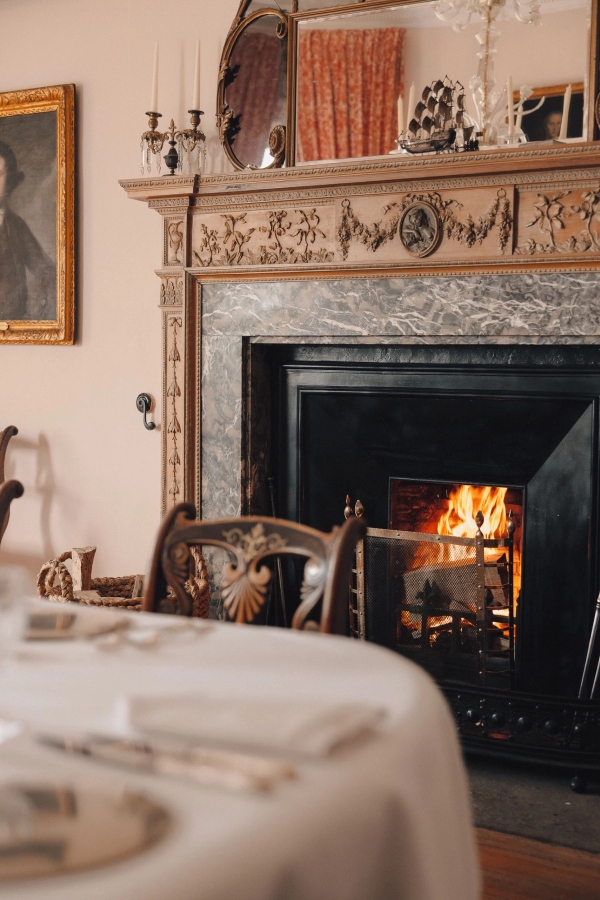 Open roaring fireplace in a historic castle reception room set with a small dining table, Love Locations KY15.