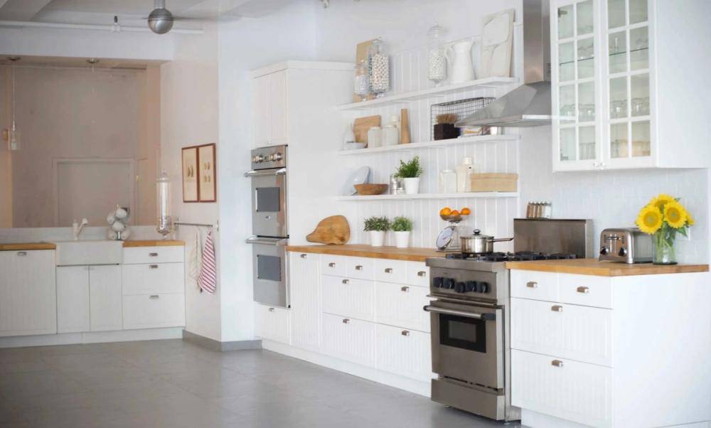 Wide shot of a clean, all-white kitchen setup with professional ovens and white cabinetry in an NYC 10011 loft location, Love Locations.