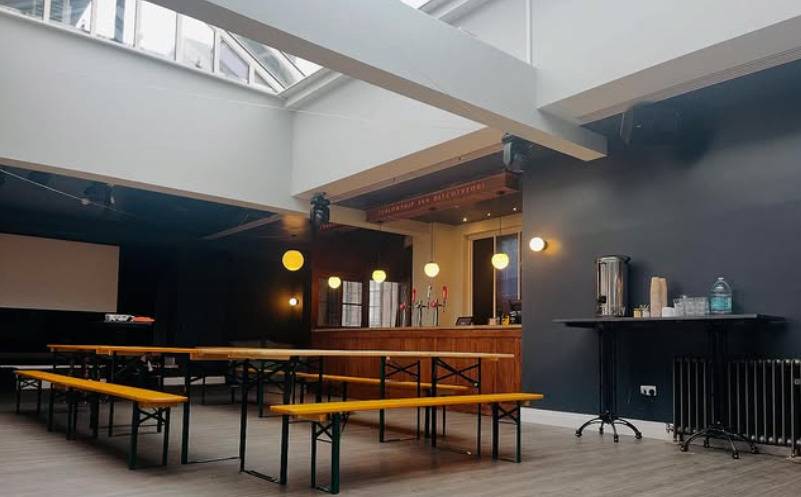 Modernist function room and bar area with long wooden bench seating under white skylight wells in Lewisham SE6 by Love Locations.