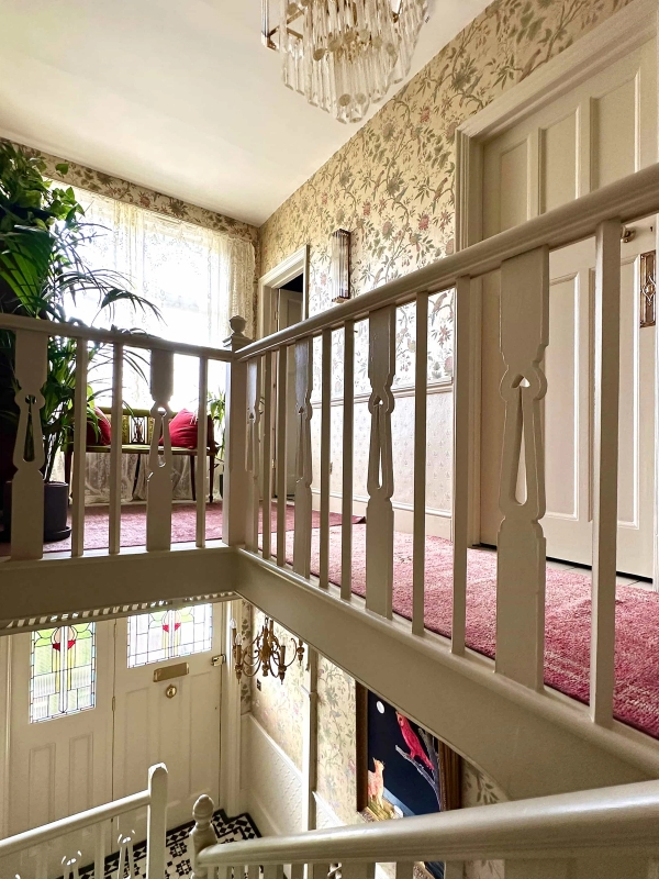 First-floor staircase landing with wooden balustrades, patterned wallpaper, and potted house plants, Love Locations N13.