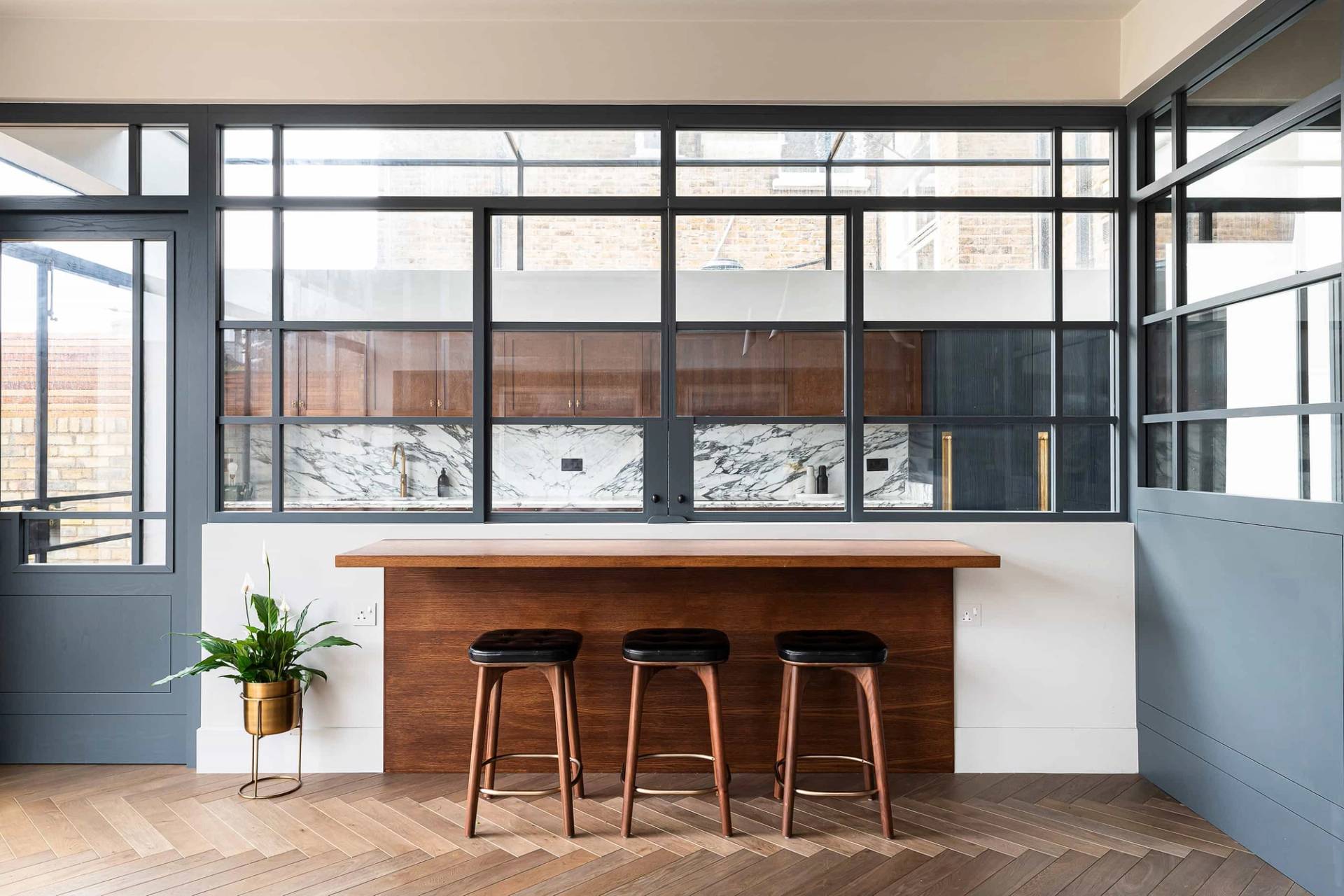 Open-plan kitchen island breakfast bar featuring dark wood counters, brass trim, and high wooden bar stools in Queens Park, ideal for food editorial filming, Love Locations NW6.