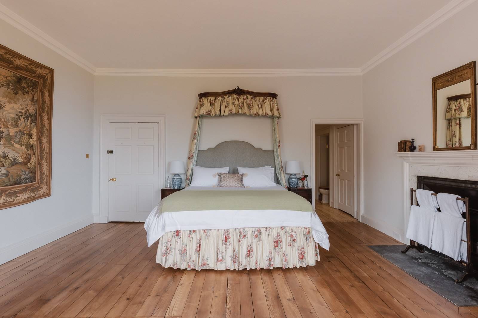 Grand white bedroom suite with an upholstered canopy bed and original timber floorboards, Love Locations KY15.