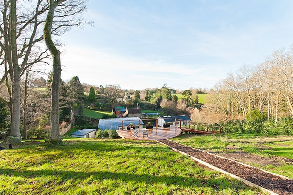 Wide landscape perspective of a modern curved-roof property built into a lush green sloping hill in Surrey, GU5, through Love Locations.