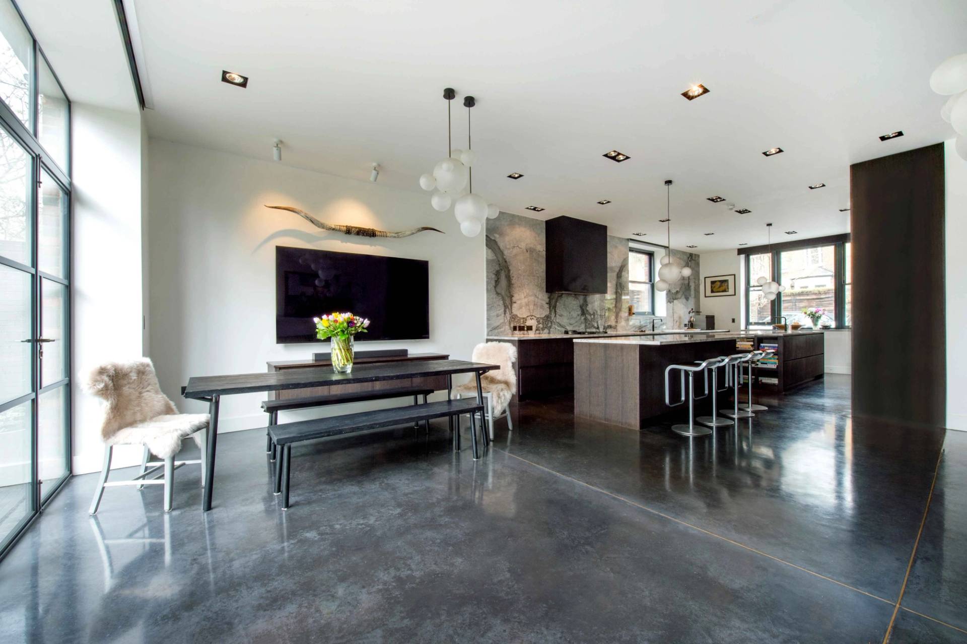Large open-plan kitchen and dining space featuring a long dark wood dining table, polished concrete floors, and modern kitchen island, Love Locations NW3.